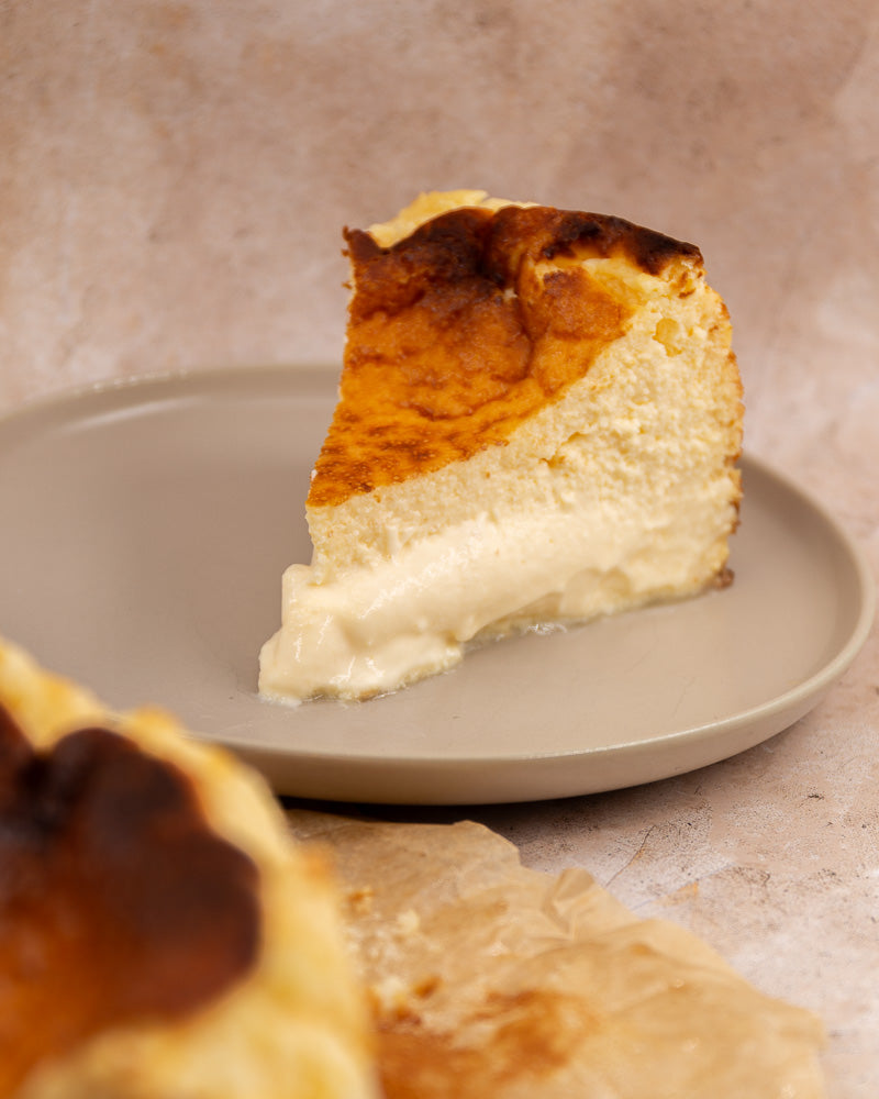 Porción de tarta de queso grande con una textura cremosa y un dorado perfecto, servida en un plato beige