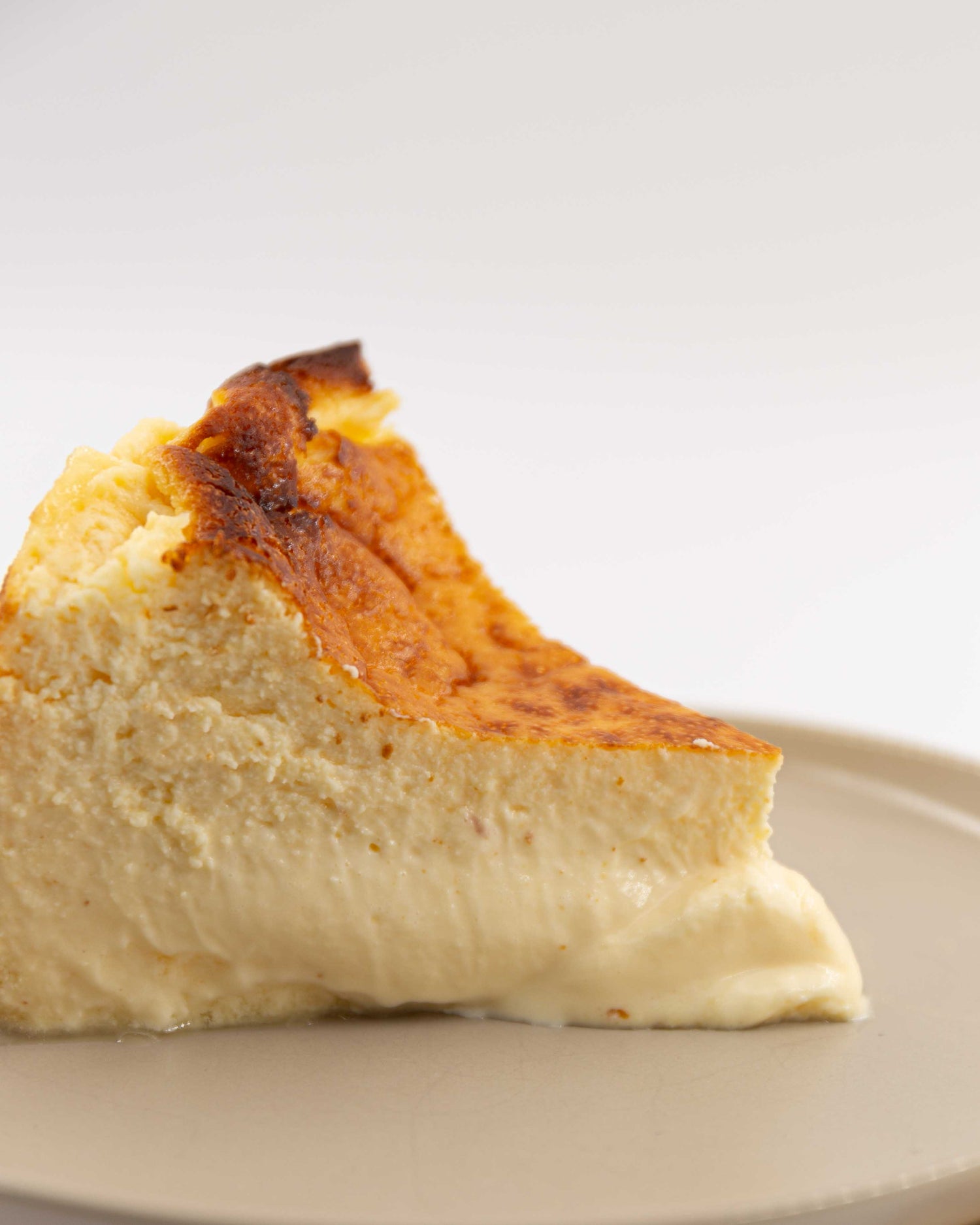 Porción de tarta de queso grande con textura cremosa y dorado uniforme, servida en un plato beige, disponible en el barrio de Salamanca